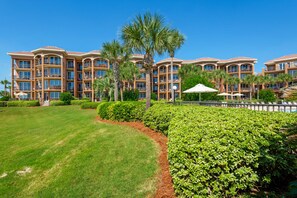 A multi-story hotel with balconies, palm trees, and a well-maintained lawn. - BeachFront! Pool, Grill, Beach Svc! wifi, kitchen (Miramar Beach)
