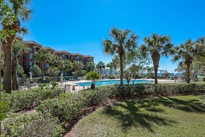 A resort with a swimming pool, palm trees, and a building with balconies. - BeachFront! Pool, Grill, Beach Svc! wifi, kitchen (Miramar Beach)