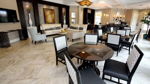 A spacious dining area with round tables and black chairs, a living area with a sofa and a TV, and a modern ceiling design. - 7163 Solterra (Davenport)