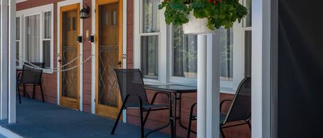 A covered porch with a table and chairs, a hanging flower basket, and a door with a number 22.