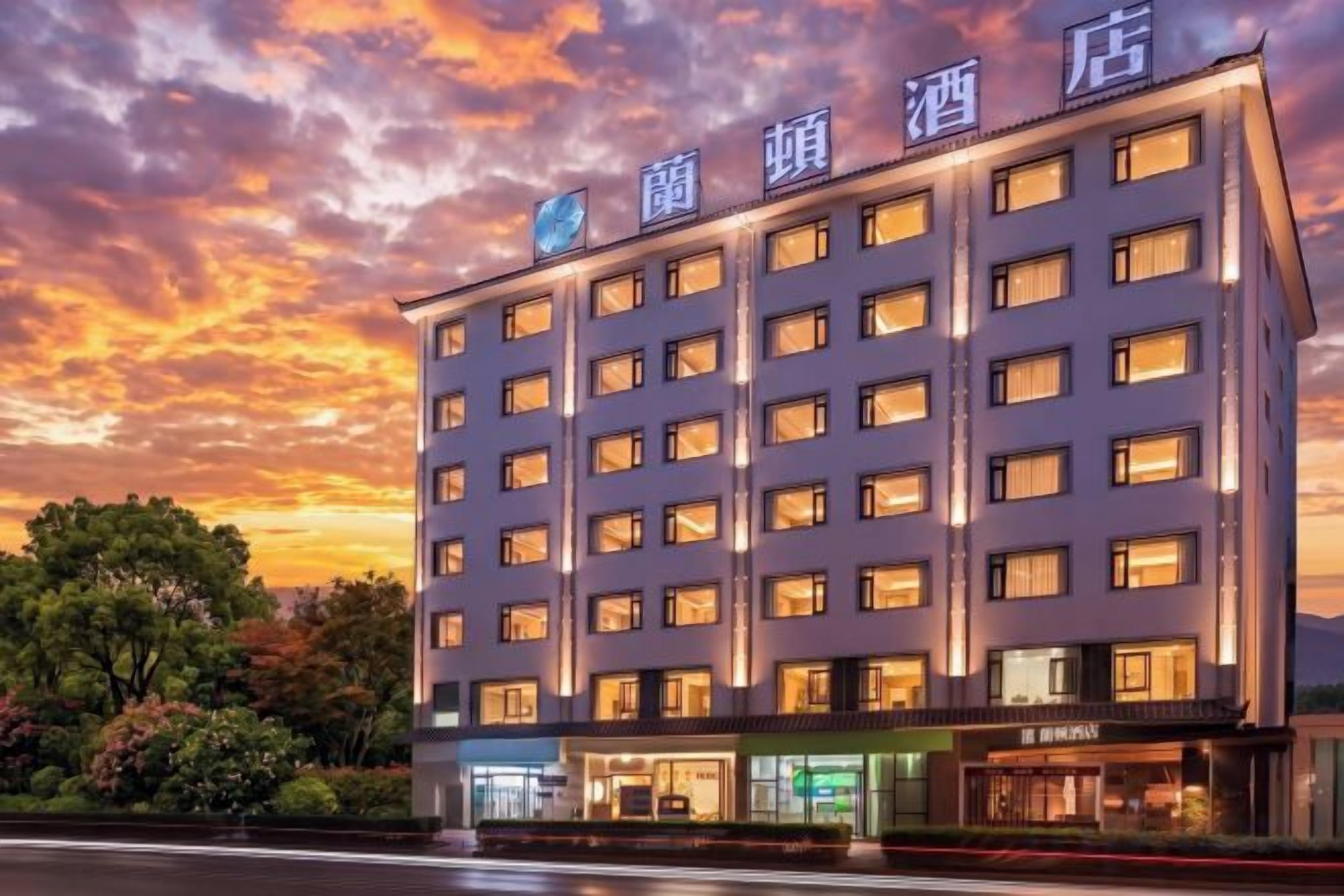 A multi-story hotel building with a row of windows on each floor, a ground-level entrance, and signage above the entrance.
