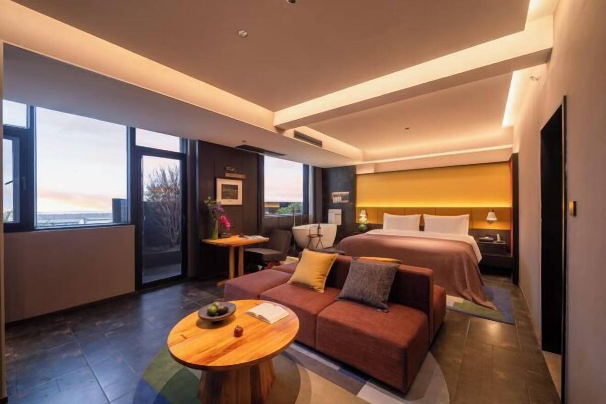 Een moderne hotelkamer met een groot bed, een slaapbank, een tafeltje en uitzicht op de stad.
