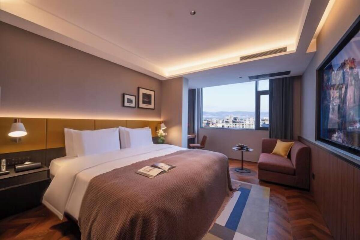 Een hotelkamer met een groot bed, een kleine zithoek, een bureau en uitzicht op de stad.