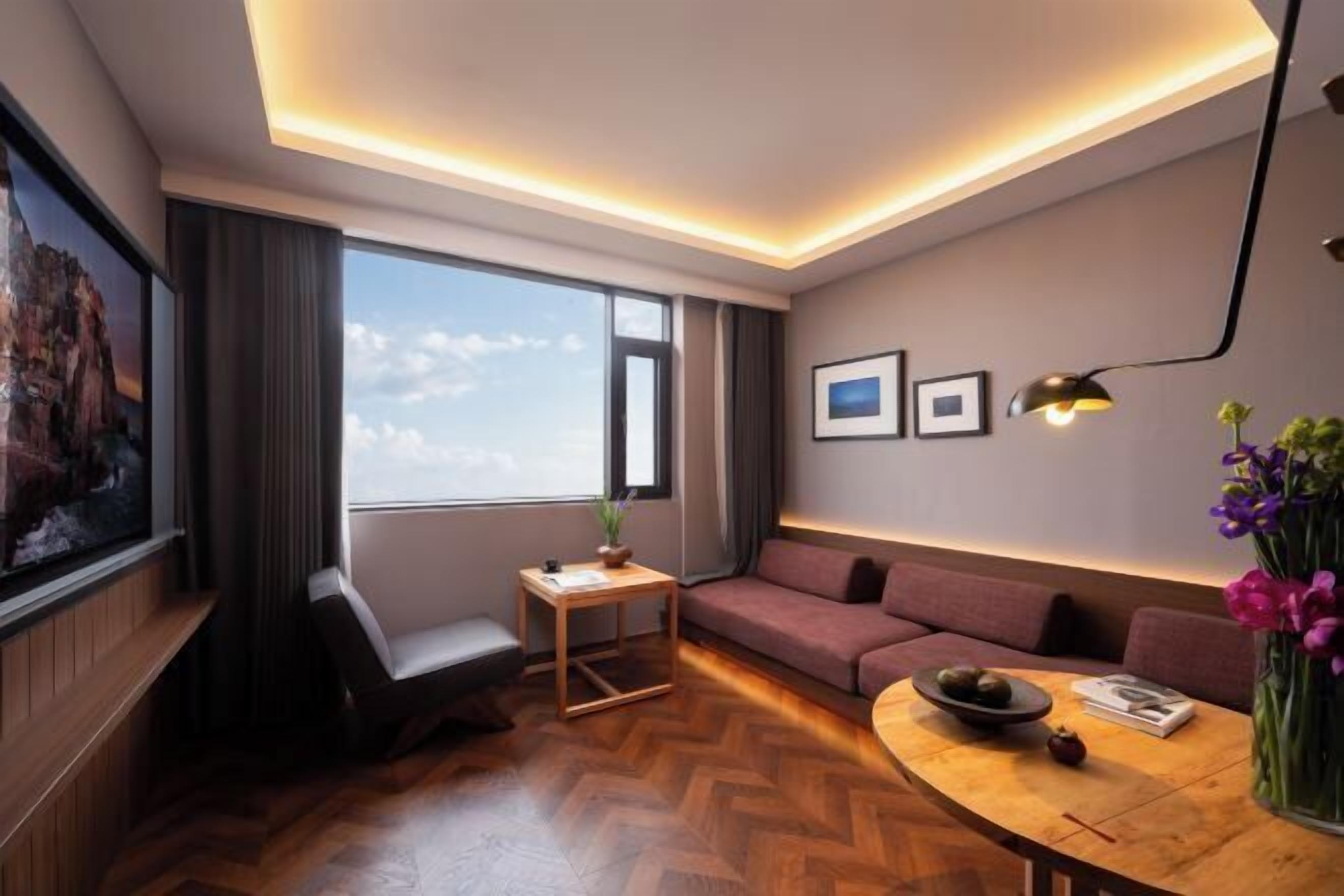 A modern living room with a sofa, a small table, a chair, a large window, and a wall-mounted lamp.