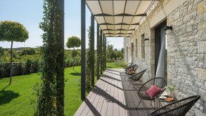 Un patio exterior cubierto con paredes de piedra, suelo de madera y sillas de mimbre negro con cojines.