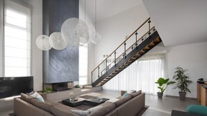 Una sala de estar moderna con un amplio sofá modular, una chimenea, una escalera y un gran ventanal.