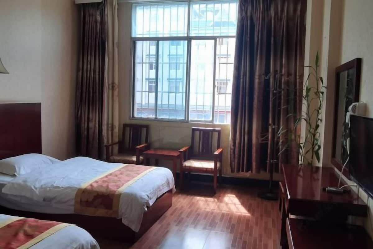 A hotel room with two beds, a small table, a chair, a TV, and a window with curtains.