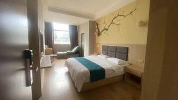 A hotel room with a large bed, a desk, a chair, and a window with curtains.