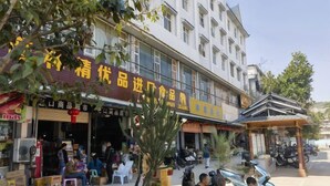 A building with multiple shops on the ground floor and a parking area in front. - Yintai Hotel (Menglian)