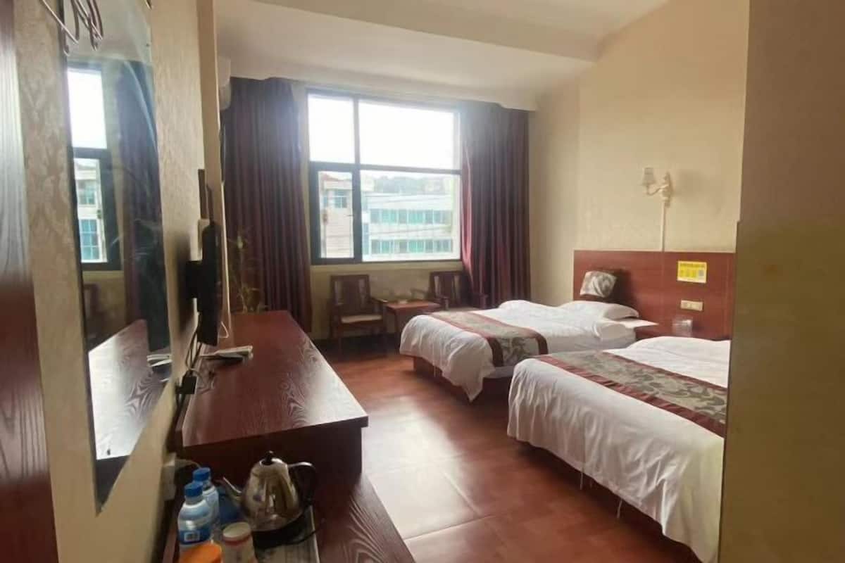 A hotel room with two single beds, a wooden desk with a chair, a television, and a window with curtains.
