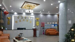 A hotel lobby with a reception desk, a coffee table, leather sofas, a chandelier, and a decorative plant arrangement. - Yintai Hotel (Menglian)