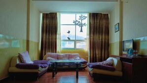 A living room with two sofas, a coffee table, and a TV on a wooden cabinet. - Yintai Hotel (Menglian)