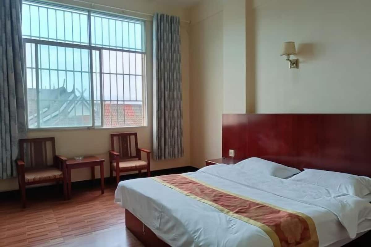 A hotel room with a large bed, two chairs, a window with curtains, and a wall-mounted lamp.