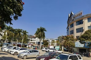 A parking lot with multiple cars, palm trees, and a building with signage. - Yintai Hotel (Menglian)