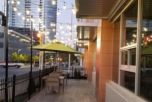 An outdoor seating area with tables and chairs, a green umbrella, and a view of a city street with buildings and traffic. - Best Western Plus (Indianapolis)