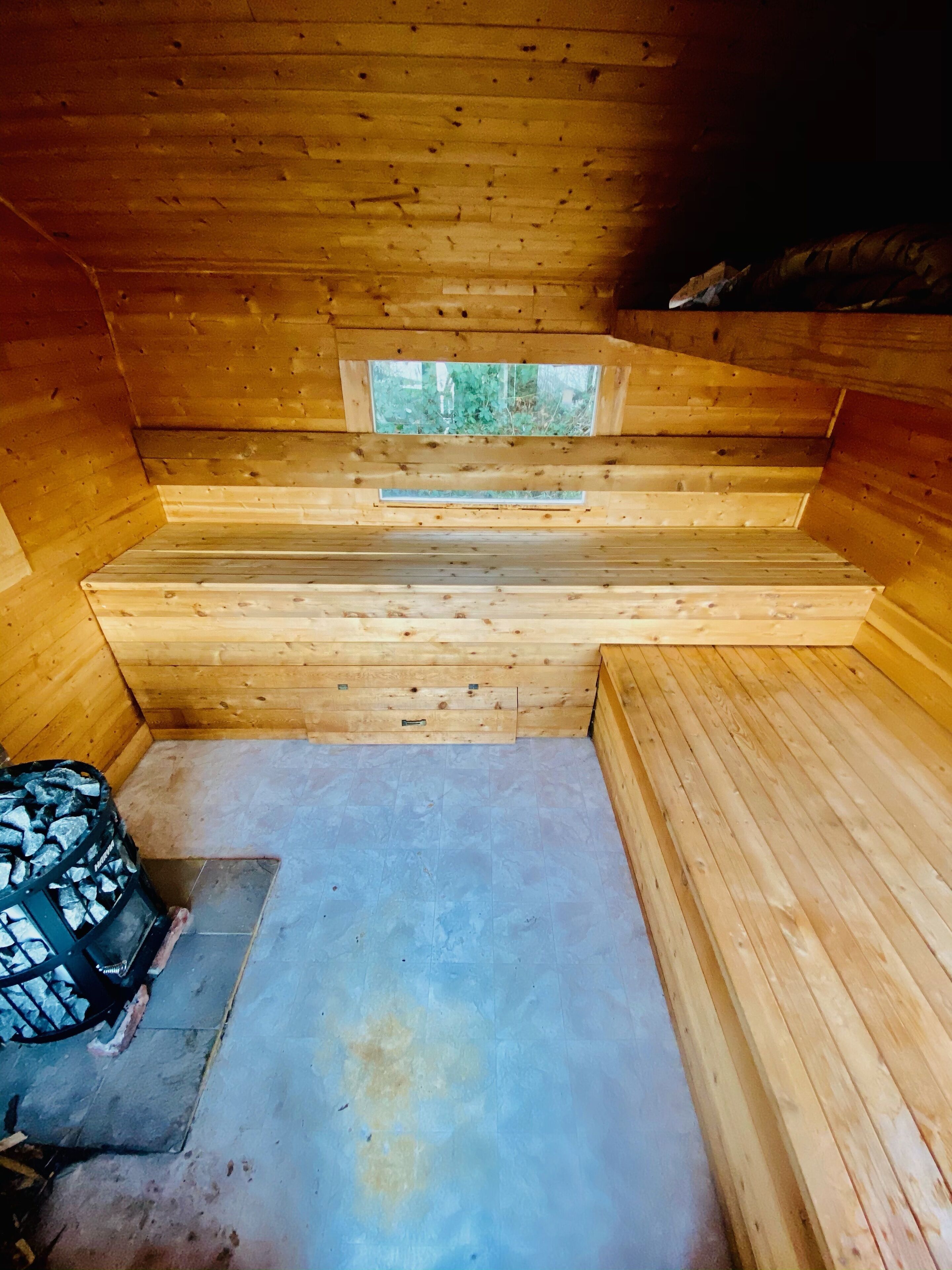 A wooden cabin interior with a bench, a small window, and a fireplace.