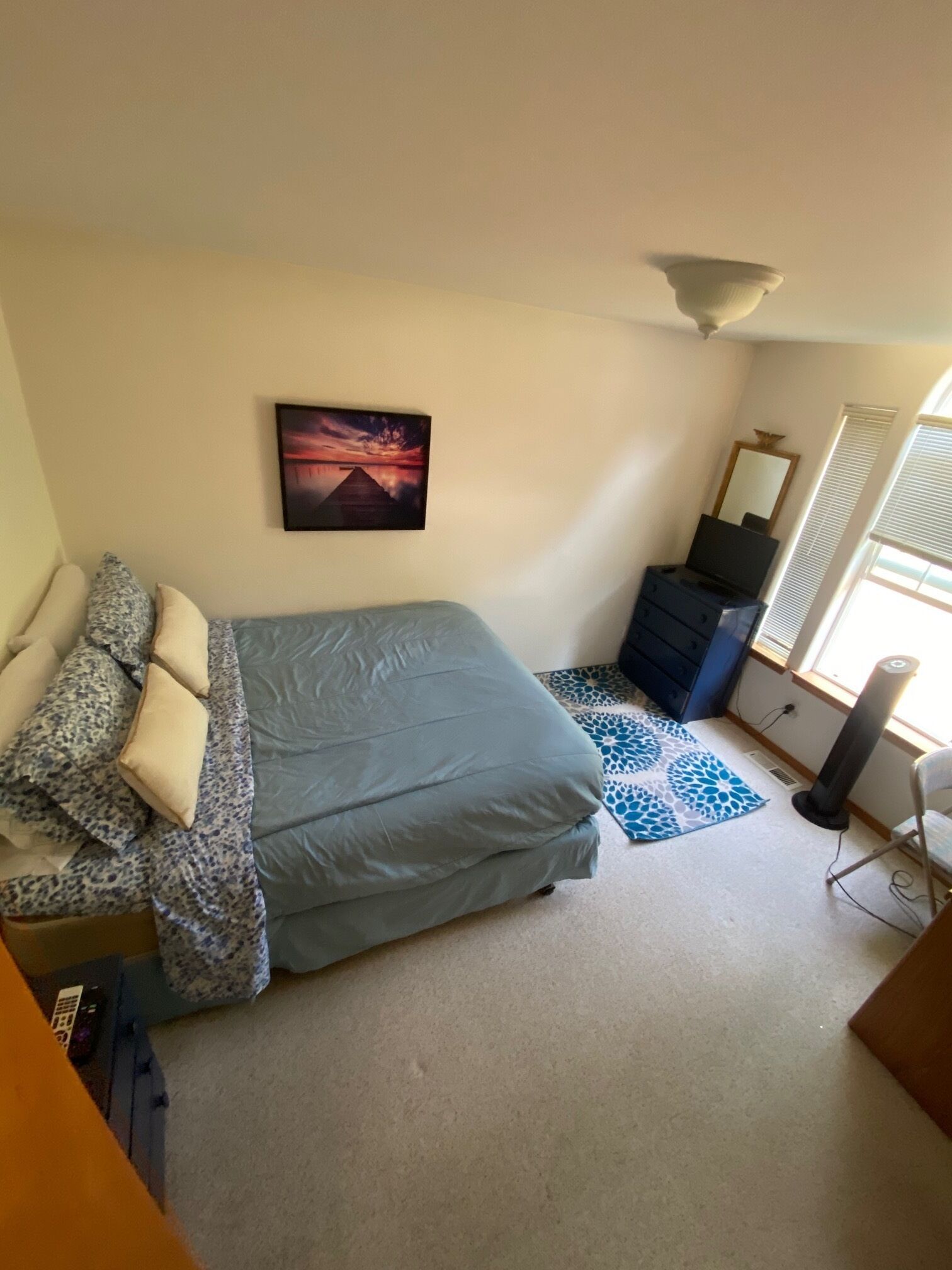 Une chambre à coucher avec un lit, une commode, un miroir, un tableau et une fenêtre.