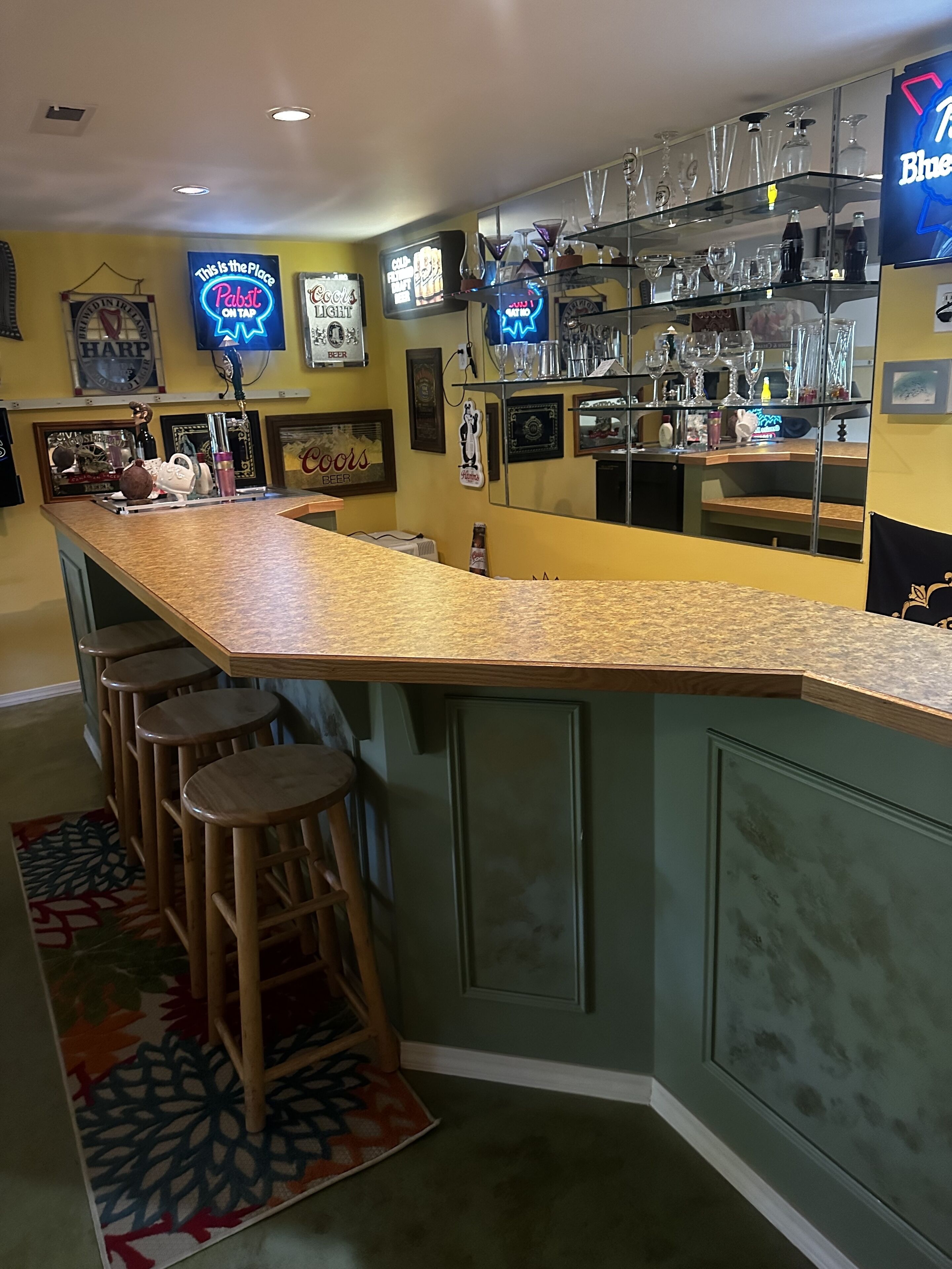 Een bar met een lange toonbank, krukken en diverse glazen en flessen.