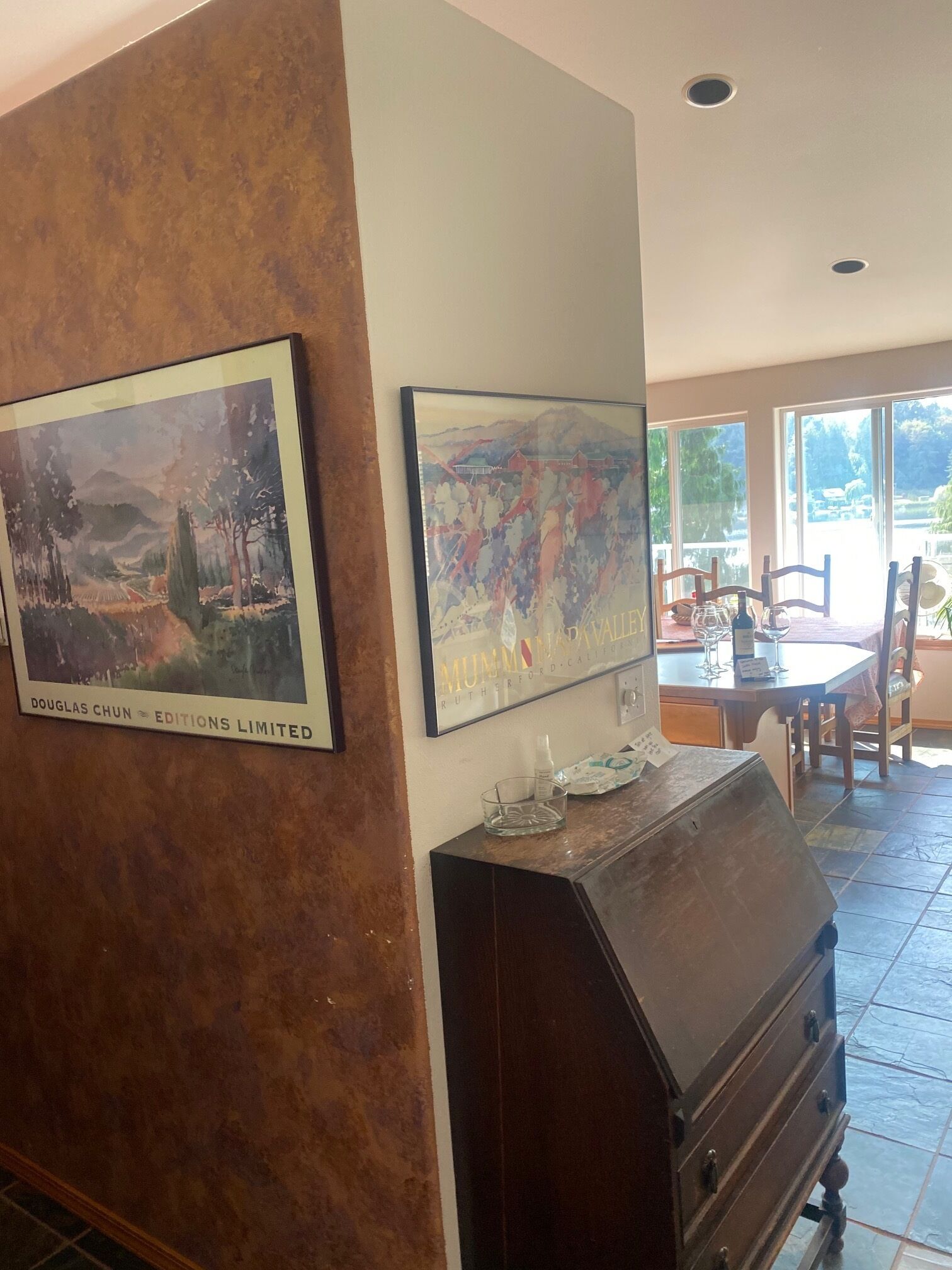 Un coin repas avec une table dressée pour deux personnes, un buffet en bois et deux œuvres d’art encadrées accrochées au mur.