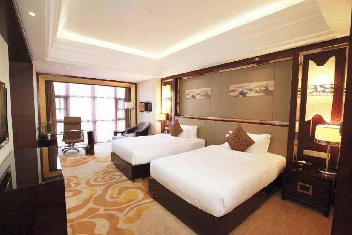 A hotel room with two beds, a desk, a chair, and a large window.