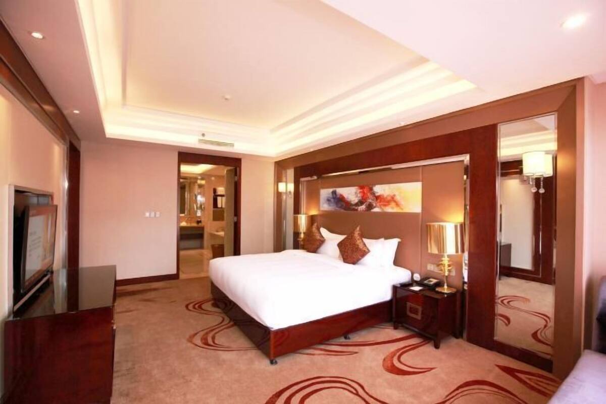 A hotel room with a large bed, a nightstand, a mirror, and a television.