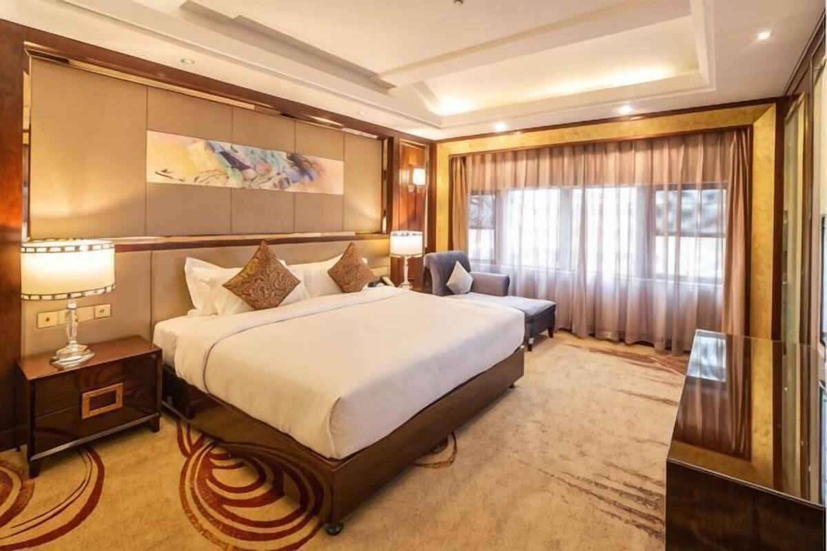 A hotel room with a large bed, a nightstand, a desk, a chair, and a large window with curtains.