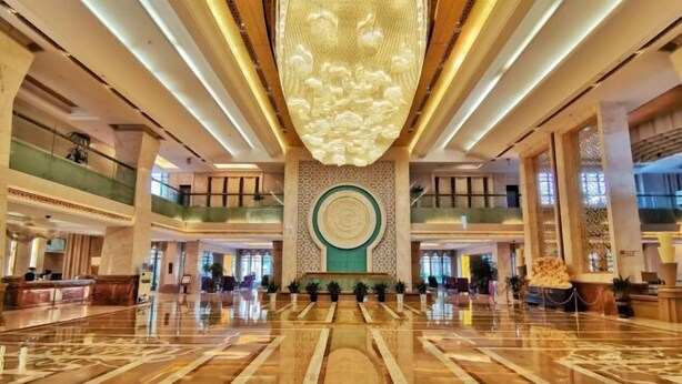 A spacious lobby with a polished marble floor, a central decorative wall, and a large chandelier.