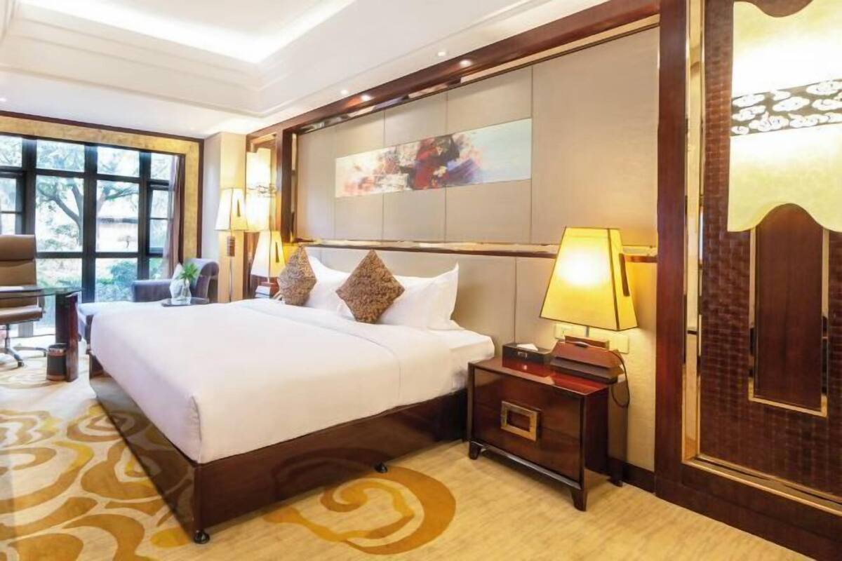 A hotel room with a large bed, a nightstand, a lamp, and a painting on the wall.