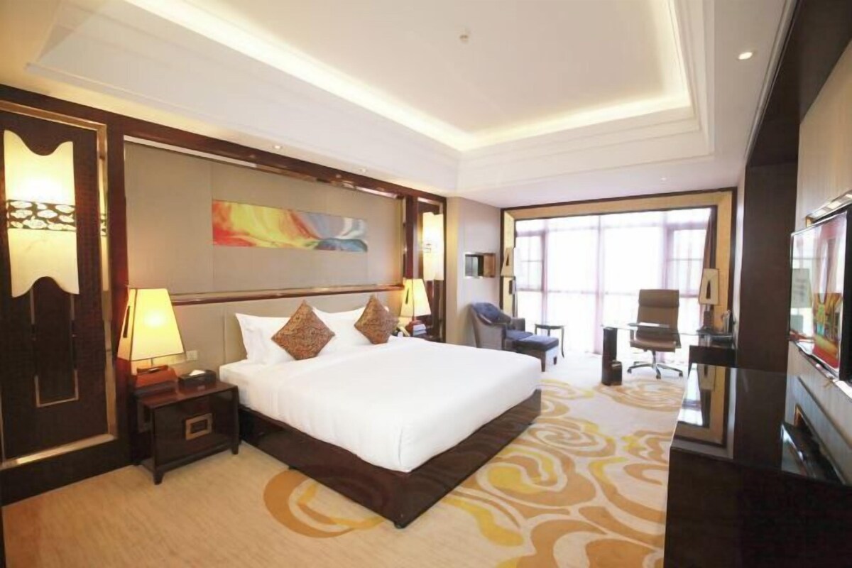 A hotel room with a large bed, a desk, a chair, a TV, and a large window.