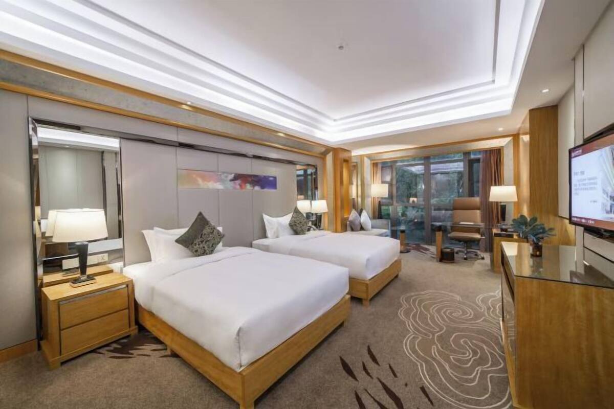 A hotel room with two beds, a desk, a TV, and a large window.
