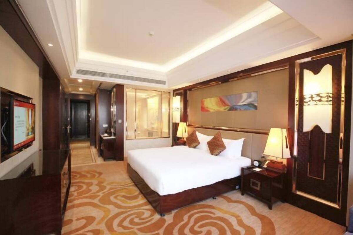 A hotel room with a large bed, a wooden headboard, a nightstand, a lamp, and a painting on the wall.