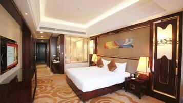 A hotel room with a large bed, a wooden headboard, a nightstand, a lamp, and a painting on the wall.