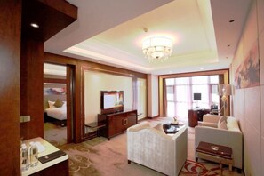 A hotel room with a bed, a desk with a computer, a TV, a sofa, and a chandelier.