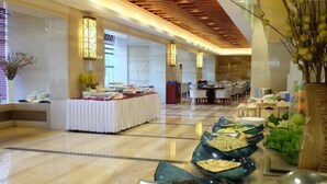 A spacious lobby with a long reception desk, a seating area with a white tablecloth, and a buffet with various dishes.