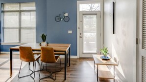 A room with a wooden table, two chairs, a potted plant, and a door with a window.