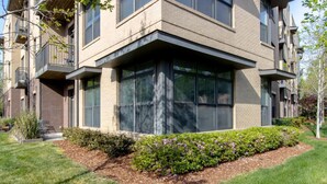 A modern multi-story building with a prominent corner entrance, large windows, and a landscaped garden area.