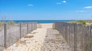 Ein sandiger Pfad führt zu einem Strand, der von einem Holzzaun an beiden Seiten gesäumt wird.