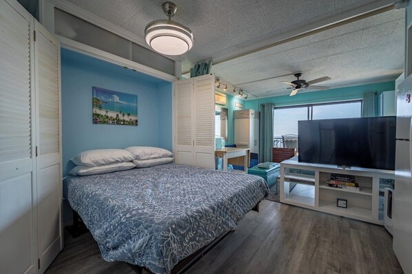 A bedroom with a bed, a TV, a ceiling fan, and a window.