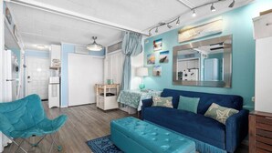 Ein gemütlicher Wohnbereich mit einem blauen Sofa, passendem Hocker, einem türkisfarbenen Sessel und einem kleinen Tisch.