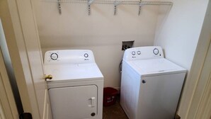 Une buanderie avec deux machines à laver blanches et un seau rouge.