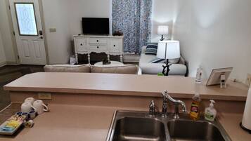 A compact kitchen with a sink, a dining area with a table and chairs, a television, and a window with curtains.
