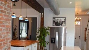 Cozinha com parede de tijolos, bancada de madeira, geladeira de aço inoxidável e luminárias pendentes.