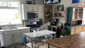 Uma cozinha moderna com armários brancos, uma pia de aço inoxidável, micro-ondas e uma ilha grande com bancada de madeira.