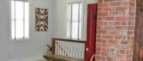 A spacious room with wooden flooring, a bench, a red door, and a brick column.