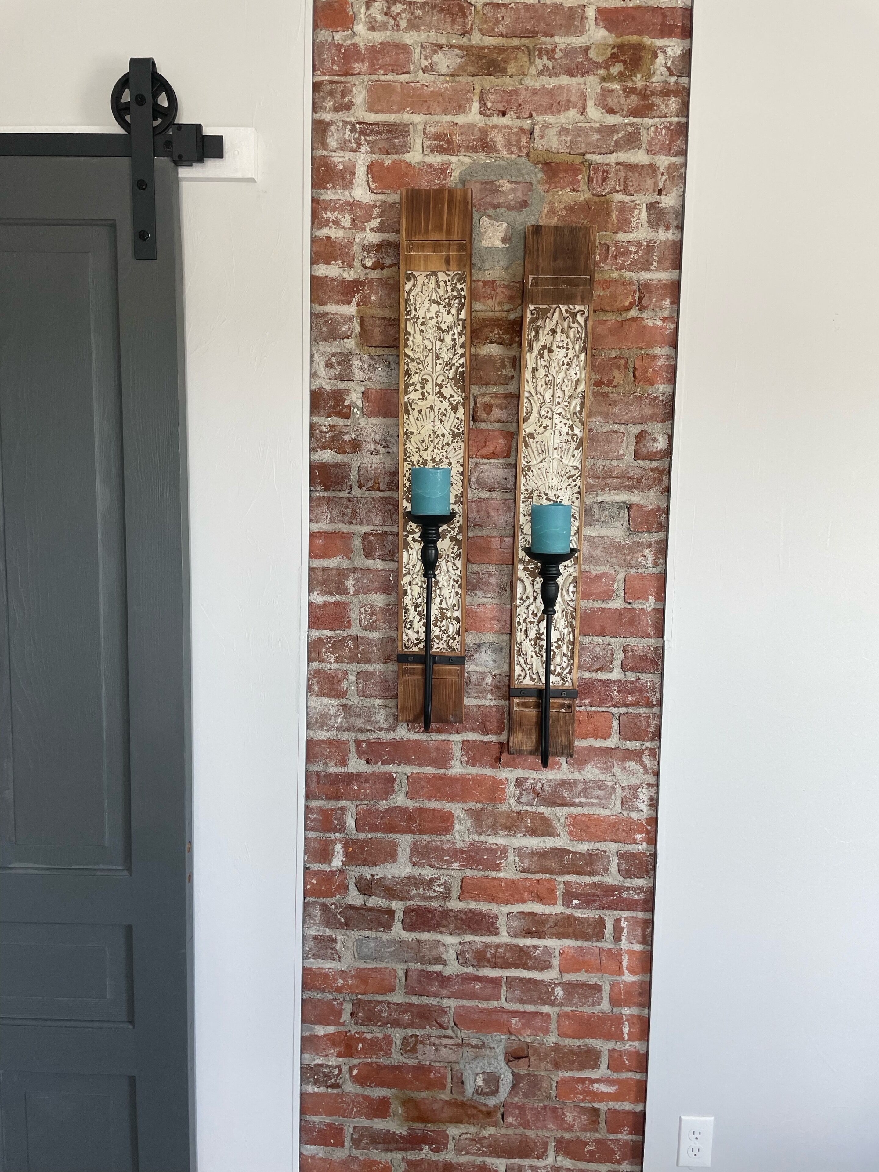 A room with a brick wall, a sliding door, and two wall-mounted sconces with teal candles.