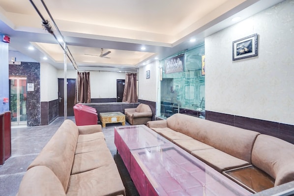 A hotel lobby with beige sofas, a glass coffee table, a ceiling fan, and a framed picture on the wall.