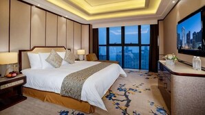 Habitación de hotel con una cama grande, televisión, escritorio y vistas a la ciudad.