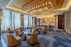 A hotel lobby with round tables, sofas, a bar area, and patterned carpet. - Grand New Century Hotel (Zhangshu)