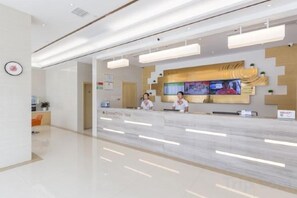 Zona de recepción de un hotel, con un mostrador de mármol, un escritorio de recepción y una pantalla de televisión que muestra un programa.