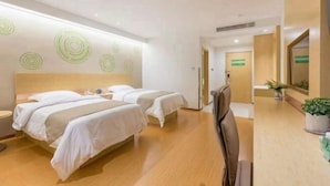 A hotel room with two beds, a wooden floor, a desk, and a mirror.